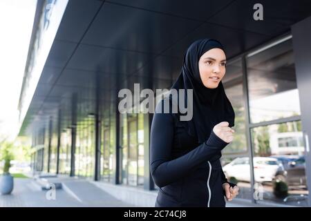 Junge muslimische Sportlerin im Hijab läuft in der Nähe von Gebäude Stockfoto