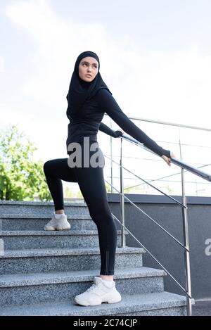 Junge muslimische Sportlerin im Hijab, die draußen auf Treppen steht Stockfoto