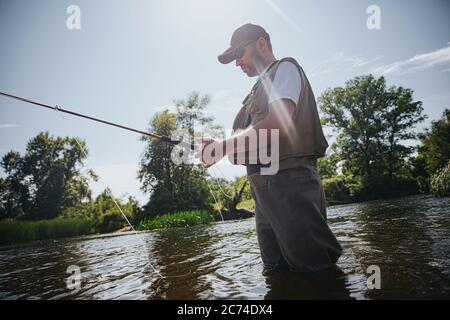 Junge Fischer fischen auf See oder Fluss. Erwachsener Kerl in Fischerkleidung und Mütze, der Stange in den Händen hält. Mit Köder für den Fang von Fischen. Mand steht ein Stockfoto