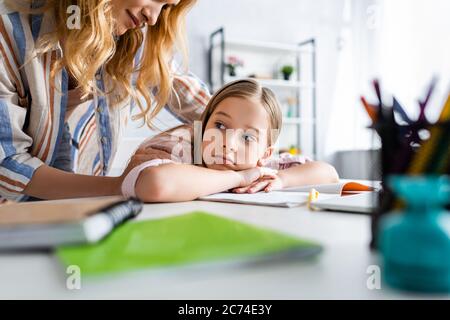 Selektiver Fokus der Mutter umarmt traurige Tochter in der Nähe Schreibwaren auf dem Tisch Stockfoto