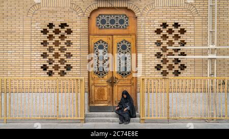 Qom, Iran - Mai 2019: Iranische Frau sitzt an einer Tür in der heiligen Stadt Qom, die von schiitischen Muslimen als die zweitheiligste Stadt angesehen wird Stockfoto