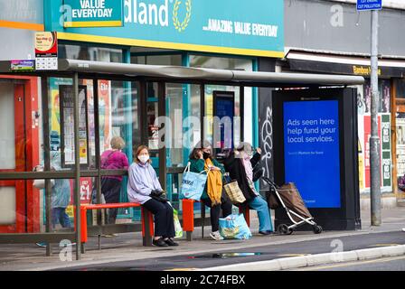 Brighton UK 14. Juli 2020 - Käufer warten heute an einer Bushaltestelle in den Straßen von Brighton mit Gesichtsmasken . Ab Freitag, 24. Juli wird es für Menschen obligatorisch, Gesichtsmasken oder Abdeckungen in Geschäften in England tragen und sie könnten Geldstrafen von bis zu £100 für Nichteinhaltung erhalten. Die neuen Regeln werden eingeführt, um im Kampf gegen Coronavirus COVID-19 Pandemie zu helfen : Credit Simon Dack / Alamy Live News Stockfoto