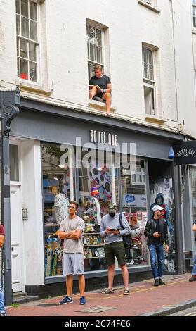 Brighton UK 14. Juli 2020 - dieser Kerl nimmt es leicht in seinem Fenster, als Käufer unter einigen tragen Gesichtsmasken in Brighton passieren . Ab Freitag, 24. Juli wird es für Menschen obligatorisch, Gesichtsmasken oder Abdeckungen in Geschäften in England tragen und sie könnten Geldstrafen von bis zu £100 für Nichteinhaltung erhalten. Die neuen Regeln werden eingeführt, um im Kampf gegen Coronavirus COVID-19 Pandemie zu helfen : Credit Simon Dack / Alamy Live News Stockfoto