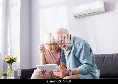 Positives Senior Coupé mit digitalem Tablet auf dem Sofa zu Hause Stockfoto