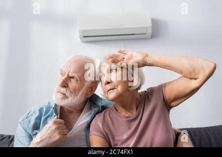 Müde ältere Pärchen, die weg schauen, während sie sich heiß auf der Couch unter der Klimaanlage fühlen Stockfoto