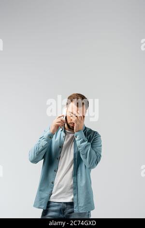 Verwirrt junger Mann auf Smartphone reden und zeigt facepalm isoliert auf grau Stockfoto