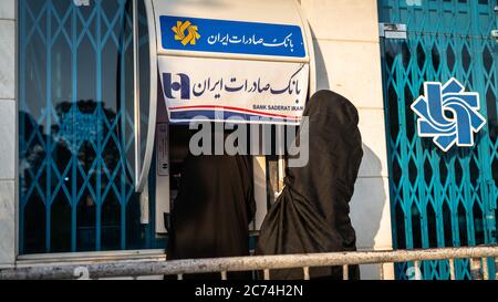 Kashan, Iran - Mai 2019: Unbekannte iranische Frauen in Hijab und Burka mit Straßenautomaten der Bank Saderat Stockfoto