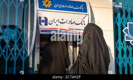 Kashan, Iran - Mai 2019: Unbekannte iranische Frauen in Hijab und Burka mit Straßenautomaten der Bank Saderat Stockfoto