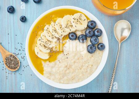 Haferflocken mit Bananen, Heidelbeeren, Chiasamen, Marmelade auf blauem Holzhintergrund Stockfoto