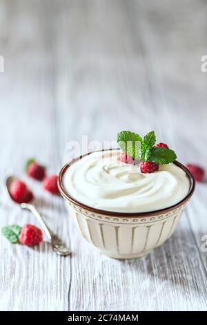 Griechischer Joghurt in einer Keramikschale auf einem hellen Holztisch. Selektiver Fokus, Kopierbereich Stockfoto