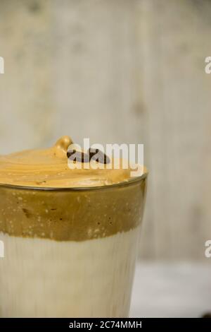 Nahaufnahme von geschlagenem Instant-Kaffee mit zwei Kaffeebohnen auf einem Glas Milch mit verschwommenem Hintergrund. Dalgona Kaffee Konzept Stockfoto