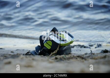 Maske zum Tauchen liegt auf dem Sand, das Ufer vor dem Hintergrund der Welle Stockfoto