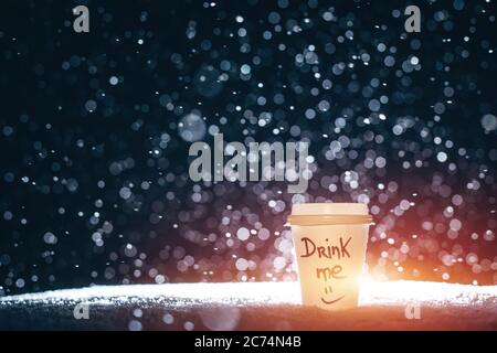Große Papiertasse mit Tee oder Kaffee auf fallendem Schnee in der Nacht Stockfoto