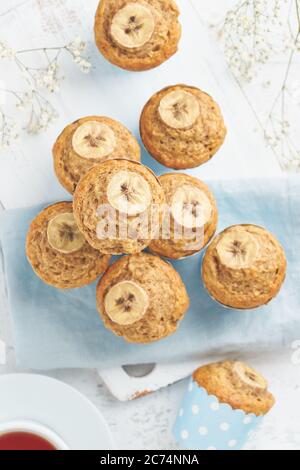 Bananenmuffin, Draufsicht, Nahaufnahme, vertikal. Frühstück auf blauer Serviette, weißer Betontisch Stockfoto