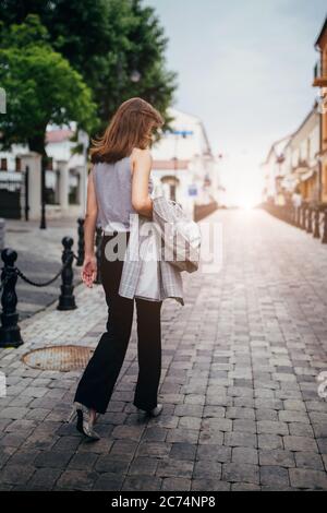 Minsk, Weißrussland - 19. Juni 2020: Ein schlankes einsames Mädchen geht mit einem Mantel in der Hand auf einer leeren Straße entlang - müde nach der Arbeit Stockfoto