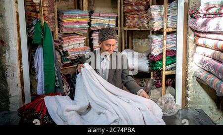 Isfahan, Iran - Mai 2019: Der alte iranische Mann verkauft in seinem kleinen Laden im Großen Basar von Isfahan Textilien Stockfoto