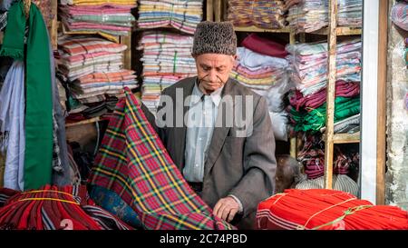 Isfahan, Iran - Mai 2019: Der alte iranische Mann verkauft in seinem kleinen Laden im Großen Basar von Isfahan Textilien Stockfoto