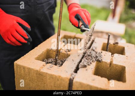 Ein professioneller Maurer baut Säulen für einen Steinzaun aus Zementblöcken - Stützzaun eines privaten Geländes Stockfoto