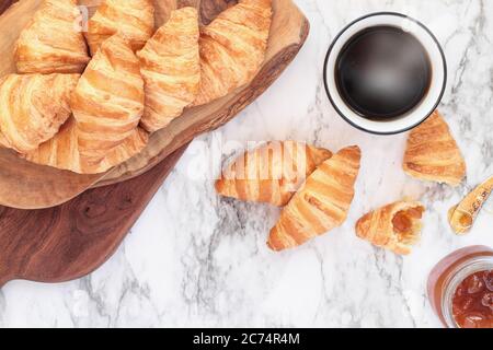 Frische, hausgemachte Croissants oder Halbmond Brötchen mit Marmelade und einer Tasse Kaffee über Marmor Hintergrundbild Schuß von der Ansicht von oben. Stockfoto
