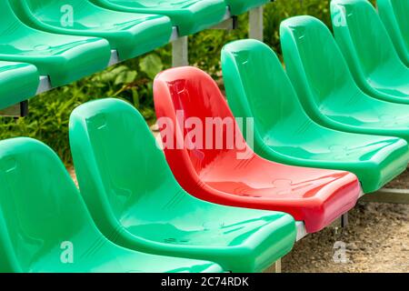 Ein roter Sitz zwischen verschiedenen Farben (grün) Sitze in einem Stadion (UNIQUE / CONFIDENCE KONZEPT) Stockfoto