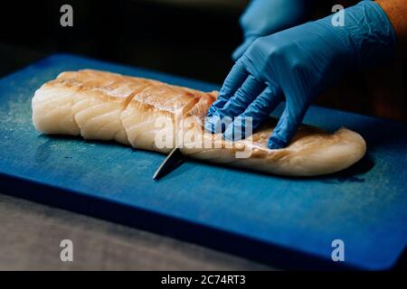 Nahaufnahme der Hände in blauen Latexhandschuhen, die rohen Fisch auf dem Schneidebrett schneiden Stockfoto