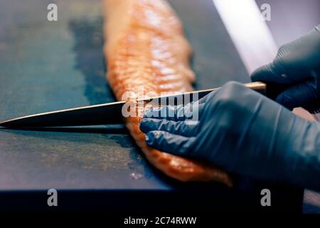 Nahaufnahme der Hände in blauen Latexhandschuhen, die Fische mit einem professionellen Messer schneiden Stockfoto