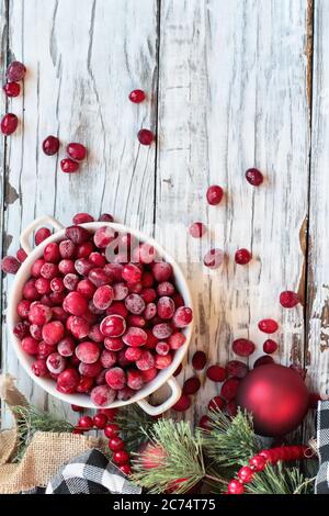 Gefrorene Cranberries in einer Schüssel über einem weißen Holz Tisch Hintergrund mit Weihnachtsschmuck. Ansicht von oben. Stockfoto