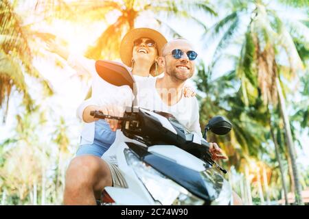 Glücklich lächelnde Paar Reisende Motorrad Scooter Reiten während ihrer tropischen Urlaub unter Palmen Stockfoto