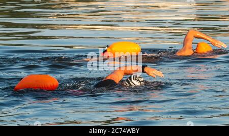 Zwei Frauen Freestyle schwimmen in Nassanzügen in der Bucht Training für Triathlons mit oranger Sicherheitsboje hinter ihnen schweben. Stockfoto