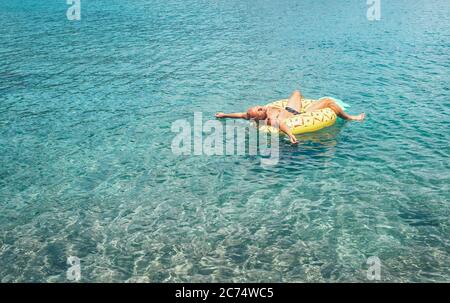 Mann entspannt beim Schwimmen auf aufblasbaren Ananas Pool Ring in kristallklarem Meerwasser. Sorgloses Urlaubskonzept Bild. Stockfoto