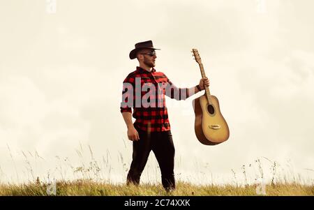 Country Music Konzept. Gitarrist Country Sänger steht im Hintergrund von Field Sky. Landhausstil. Sommerurlaub. Wanderlied. Inspirierter Country-Musiker. Vereint mit der Natur. Gutaussehender Mann mit Gitarre. Stockfoto