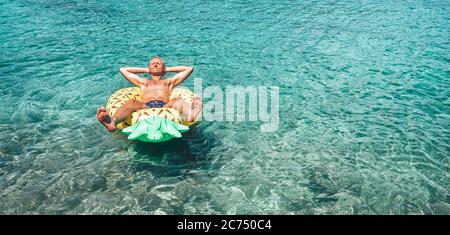 Mann entspannt beim Schwimmen auf aufblasbaren Ananas Pool Ring in kristallklarem Meerwasser. Sorgloses Urlaubskonzept Bild. Stockfoto