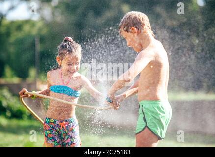 Zwei Kinder spielen im Garten, gießt sich gegenseitig aus dem Schlauch, macht einen Regen. Happy Kindheitskonzept Bild. Stockfoto