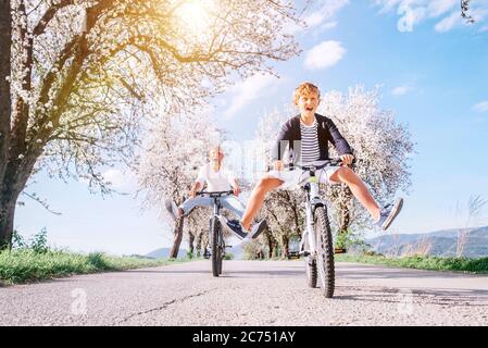 Vater und Sohn haben Spaß, breiten Beinen und Schreien beim Radfahren auf der Landstraße unter Blütenbäumen. Gesundes sportliches Lifestyle-Konzept Stockfoto