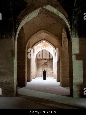 Isfahan, Iran - 2019. Mai: Unbekannte iranerin in Hijab-schwarzem Kleid, die entlang der antiken Säulen der Jameh-Moschee von Isfahan geht Stockfoto