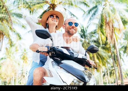 Glücklich lächelnde Paar Reisende Motorrad Scooter Reiten während ihrer tropischen Urlaub unter Palmen Stockfoto