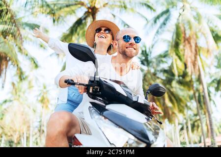 Glücklich lächelnde Paar Reisende Motorrad Scooter Reiten während ihrer tropischen Urlaub unter Palmen Stockfoto