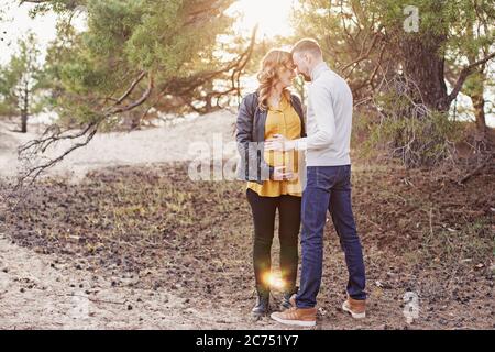 Junge glückliche Paar erwartet Baby auf ihrem Spaziergang im Park an sonnigen Tag. Warmes Licht Stockfoto