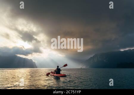 Mann auf dem Kajak, der Sonnenaufgang auf dem Cheow Lan See, Khao Sok Nationalpark, Thailand Stockfoto