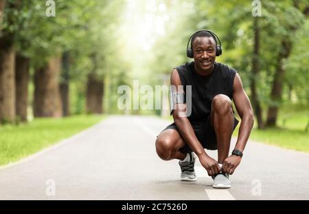 Fröhlicher afrikanischer Kerl, der vor dem Training Schnürsenkel auf seinen Sneakers bindet Stockfoto