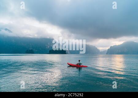 Mann schwimmt im Kajak auf Cheow Lan Lake im Khao Sok Nationalpark, Thailand Stockfoto
