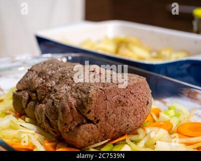 Ein traditionelles Sonntagsbraten mit einem Rinderbraten und Kartoffeln auf einer rustikalen karierten Tischdecke in einer heimischen Küche Stockfoto