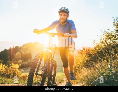 Junger lächelnder Mann, der ein Mountainbike den Hügel hinauf schiebt. Aktive Abenteuerreise mit dem Fahrrad. Stockfoto