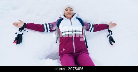 Junge lächelnde weibliche Liying auf dem weißen Schnee weit öffnete ihre Arme. Stockfoto