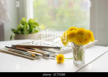 Auf dem Tisch steht ein Löwenzahn mit Farben und Pinsel zum Malen. Das Konzept der Kunst. Sommer Stillleben Stockfoto