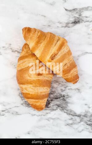 Zwei frische hausgemachte Croissants oder Halbmondrollen auf Marmorhintergrund Bild von oben. Stockfoto