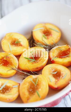 Frisch gebackene, hausgemachte Pfirsiche in braunem Zucker und frischen Rosmarinzweigen gebacken. Selektiver Fokus mit unscharfem Vorder- und Hintergrund. Stockfoto