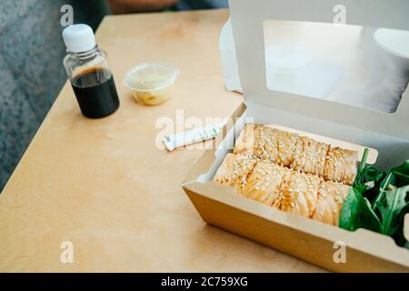 Sushi-Rollen in einem Papierbehälter auf dem Holztisch, Boxen zum Mitnehmen. Konzept Essen zum Mitnehmen. Stockfoto