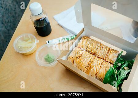 Sushi-Rollen in einem Papierbehälter auf dem Holztisch, Boxen zum Mitnehmen. Konzept Essen zum Mitnehmen. Stockfoto