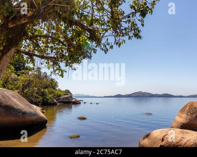 Kleiner Strand mit ruhigen Gewässern unter dem Schatten eines Baumes, große Steine und blauer Himmel, Paqueta Island, Guanabara Bay, Rio de Janeiro, Brasilien Stockfoto